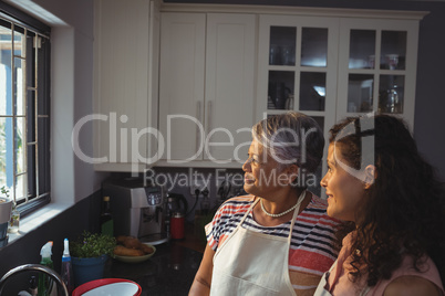 Mother and daughter looking through window in kitchen