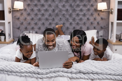 Smiling family using laptop while lying together on bed