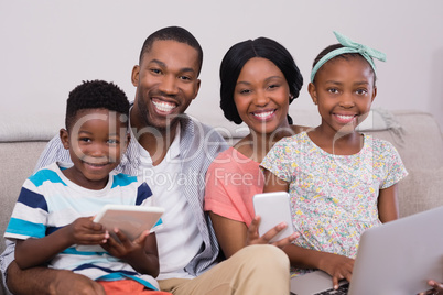 Happy family with various technologies sitting on sofa at home