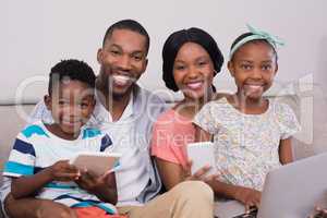 Happy family with various technologies sitting on sofa at home