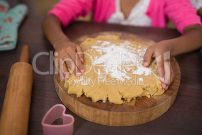 Mid section of girl touching dough in kitchen