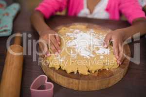 Mid section of girl touching dough in kitchen