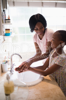 Mother looking at daughter while washing hands in bathroom