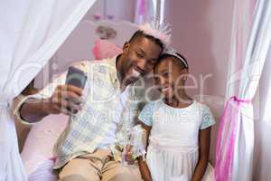 Father and daughter taking selfie while sitting on bed at home