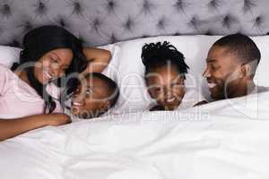 Portrait of girl lying with happy family on bed