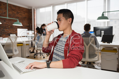 Male executive working on computer while having coffee