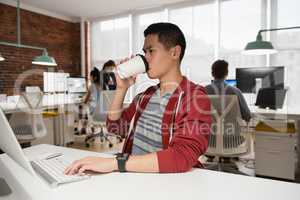 Male executive working on computer while having coffee