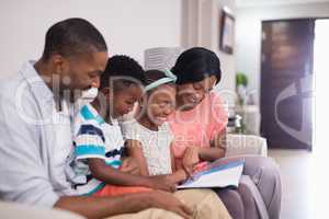 Smiling family reading magazine while sitting on sofa