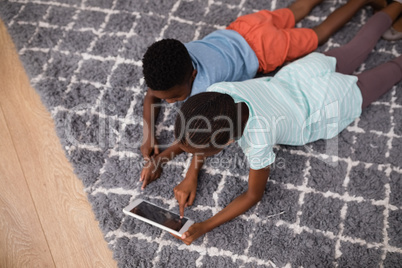 Siblings using digital tablet while lying on rug at home
