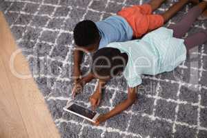 Siblings using digital tablet while lying on rug at home