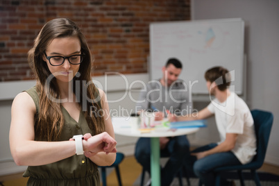 Female executive adjusting a smart watch while colleague discussing in background