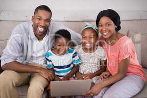 Happy family holding laptop while sitting on sofa at home
