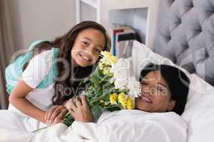 Portrait of smiling grandmother and granddaughter with flower bouquet on bed at home