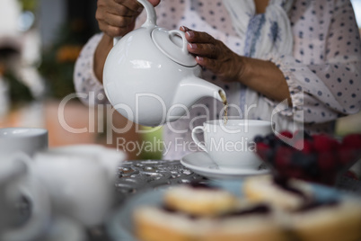 Mid section of woman pouring tea in cup