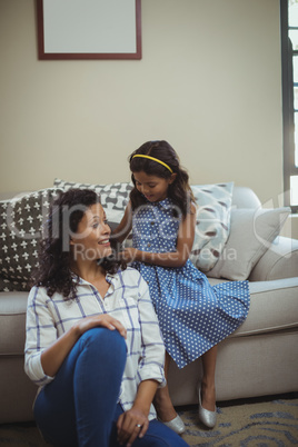 Cute daughter combing mothers hair in living room