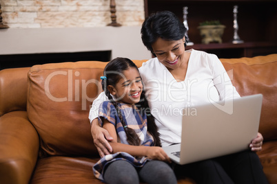 Smiling woman with granddaughter using laptop at home