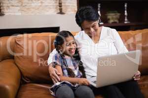 Smiling woman with granddaughter using laptop at home