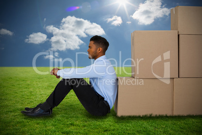 Composite image of businessman leaning on cardboard boxes against white background