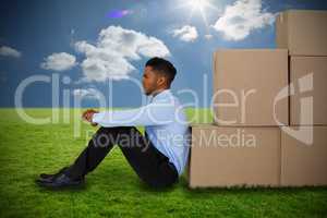 Composite image of businessman leaning on cardboard boxes against white background