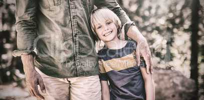 Smiling boy standing with father on sunny day in forest