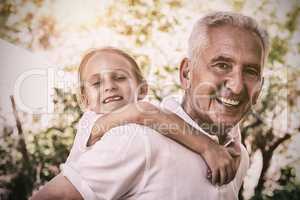 Portrait of smiling grandfather carrying granddaughter piggyback