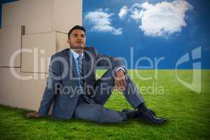 Composite image of businessman leaning on cardboard boxes against white background