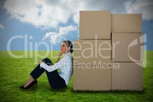 Composite image of businesswoman leaning on cardboard boxes against white background