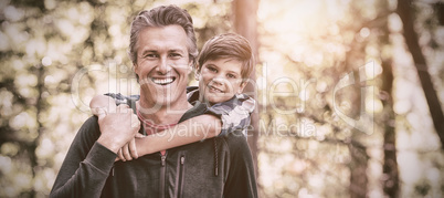 Happy father piggybacking son while hiking in forest