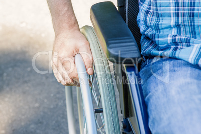 Hand of young man on the wheel of wheelchair in the city park