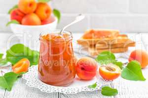 Apricot jam in a jar and fresh fruits with leaves on white wooden table, breakfast