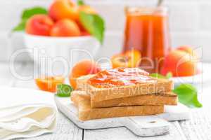 Toasts of bread with apricot jam and fresh fruit with leaves on white wooden table. Tasty breakfast.