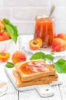 Toasts of bread with apricot jam and fresh fruit with leaves on white wooden table. Tasty breakfast.