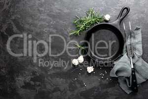 Empty cast iron frying pan on dark grey culinary background, view from above