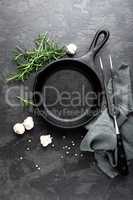 Empty cast iron frying pan on dark grey culinary background, view from above