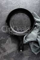 Empty cast iron frying pan on dark grey culinary background, view from above