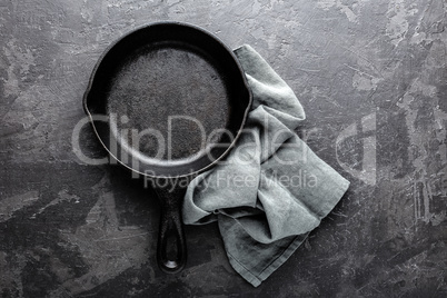 Empty cast iron frying pan on dark grey culinary background, view from above