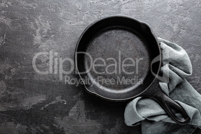 Empty cast iron frying pan on dark grey culinary background, view from above