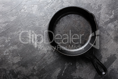 Empty cast iron frying pan on dark grey culinary background, view from above