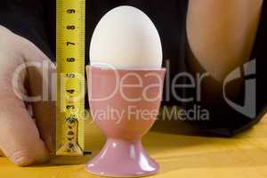 Egg in holder and hands with tape measure