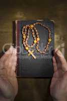 Hands with rosary and an old book