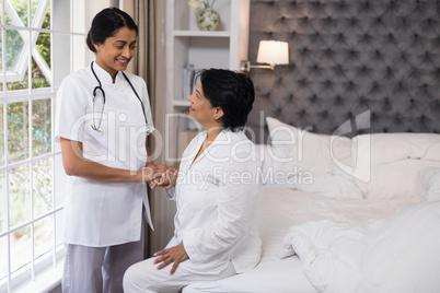 Smiling nurse comforting female patient on bed