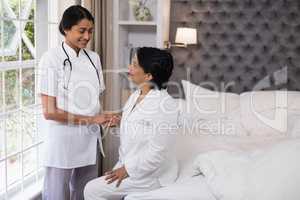 Smiling nurse comforting female patient on bed