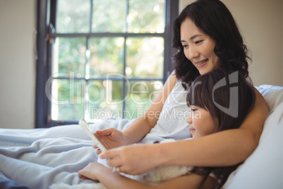 Mother and daughter using digital tablet on bed in bed room