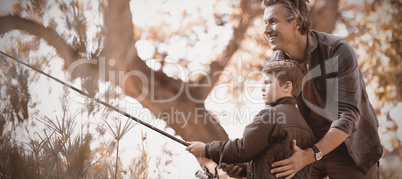 Smiling father assisting son while fishing in forest