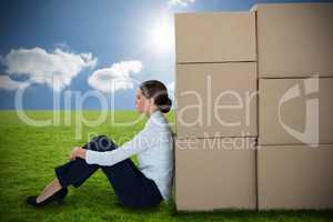 Composite image of businesswoman leaning on cardboard boxes against white background