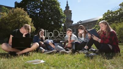 Young exhausted students learning on campus lawn