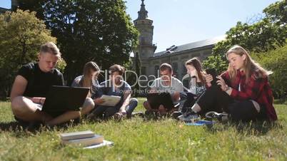 Students studying with laptop and tablet on grass