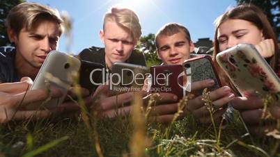 Friends in circle using smartphones on park lawn