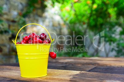 Red cherry in a yellow bucket on a brown wooden table