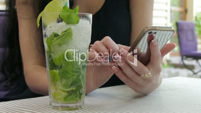 Close Up Of A Woman's Hands Using A Smartphone And Drinking A Cocktail